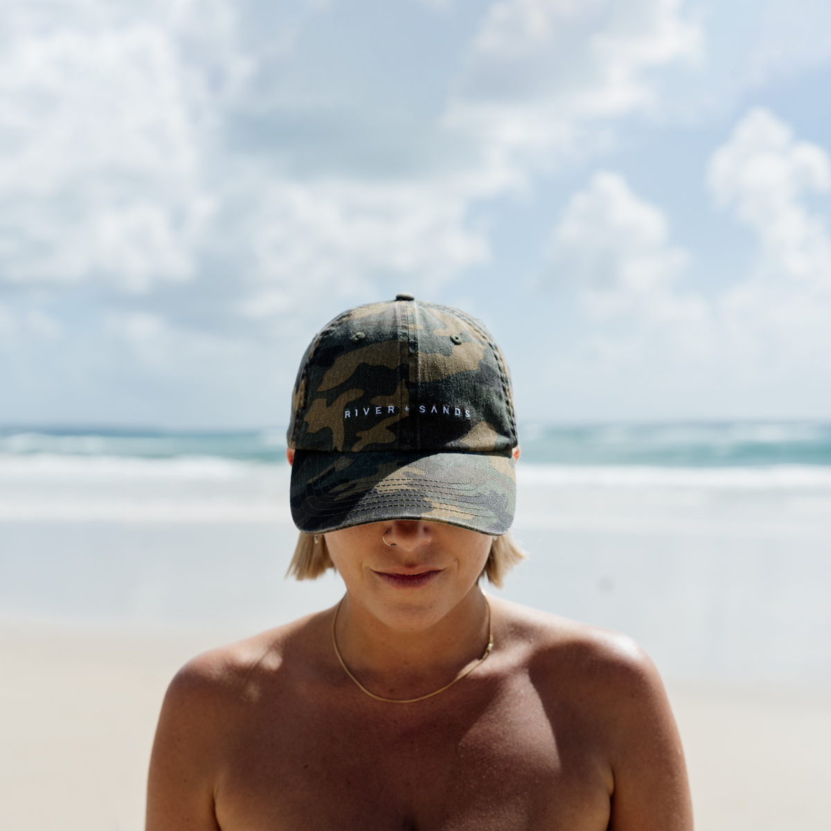 Woman wearing a camouflage cap on a beach with ocean and sky in the background