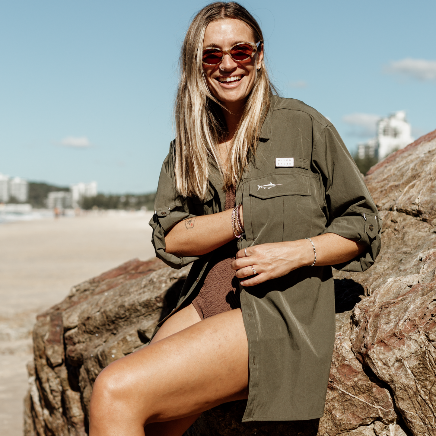 Woman wearing khaki river adventure shirt over swimmers reaching into the hidden zip pocket.