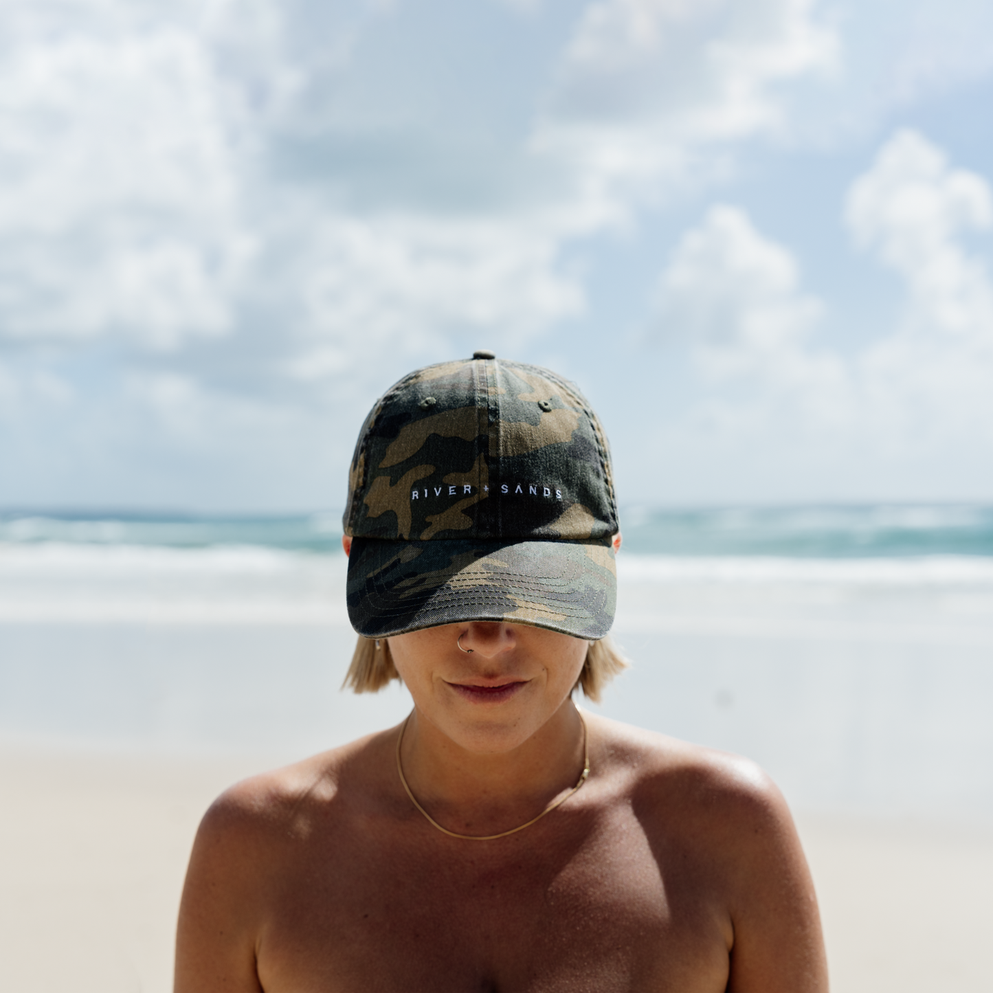 Woman wearing a camouflage cap on a beach with ocean and sky in the background