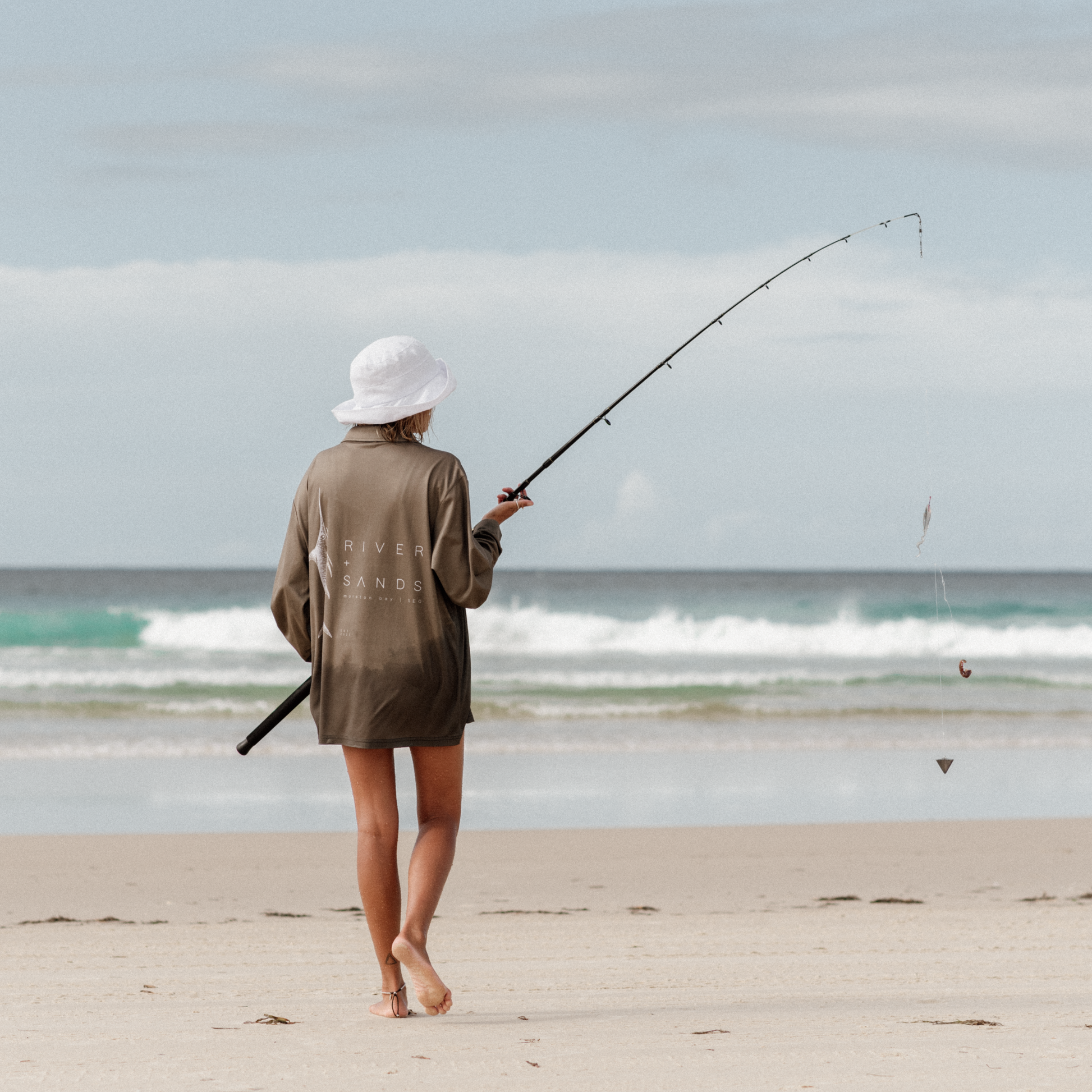 Woman walking out in her sands fishing shirt with her fishing rod for beach fishing.