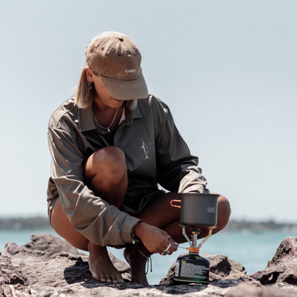 Woman making coffee on a stove wearing the sands fishing shirt.