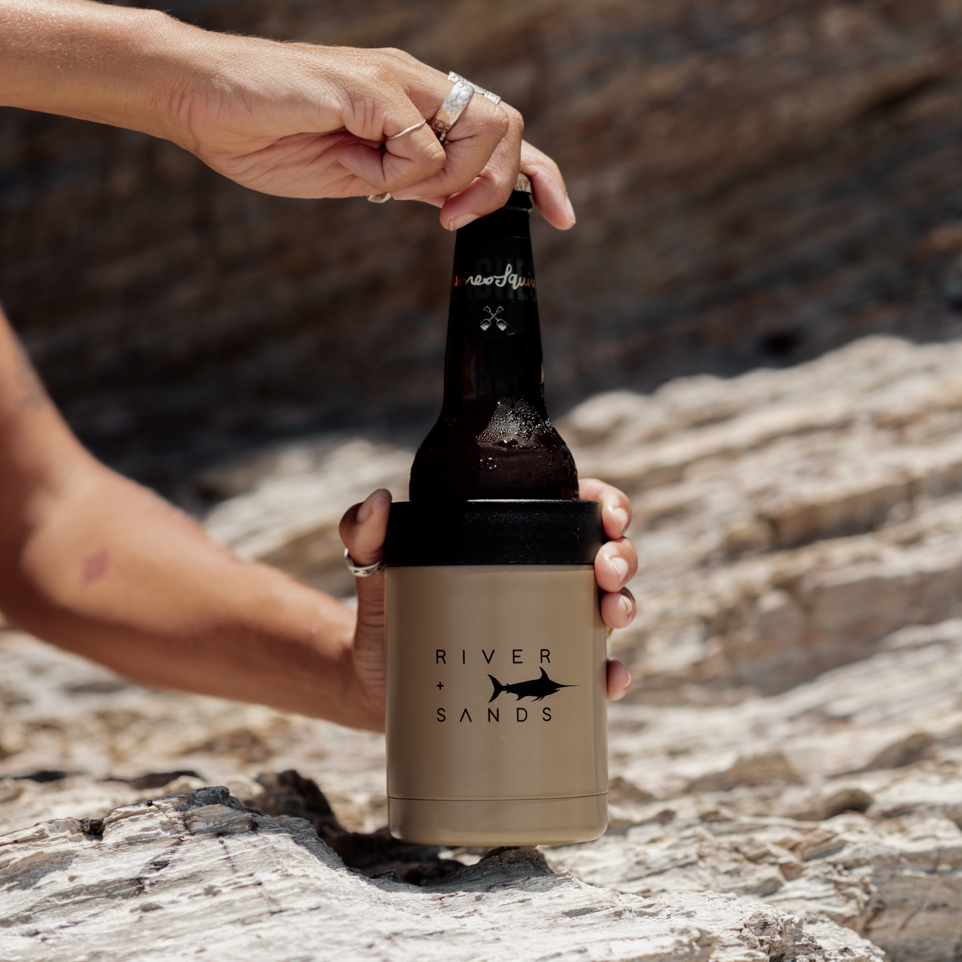 Woman reaching for her tan river and sands can cooler with rocks behind her.