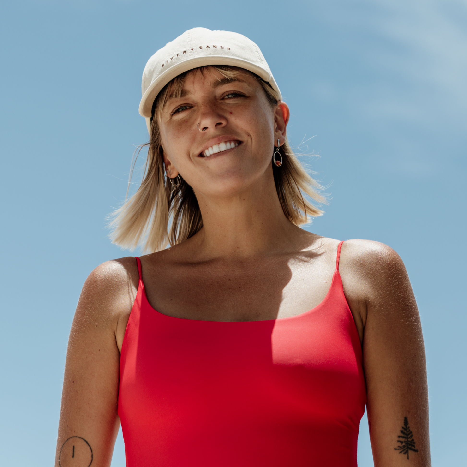 Woman smiling and wearing the beige southern Dad Cap with brown embroidery saying river and sands.