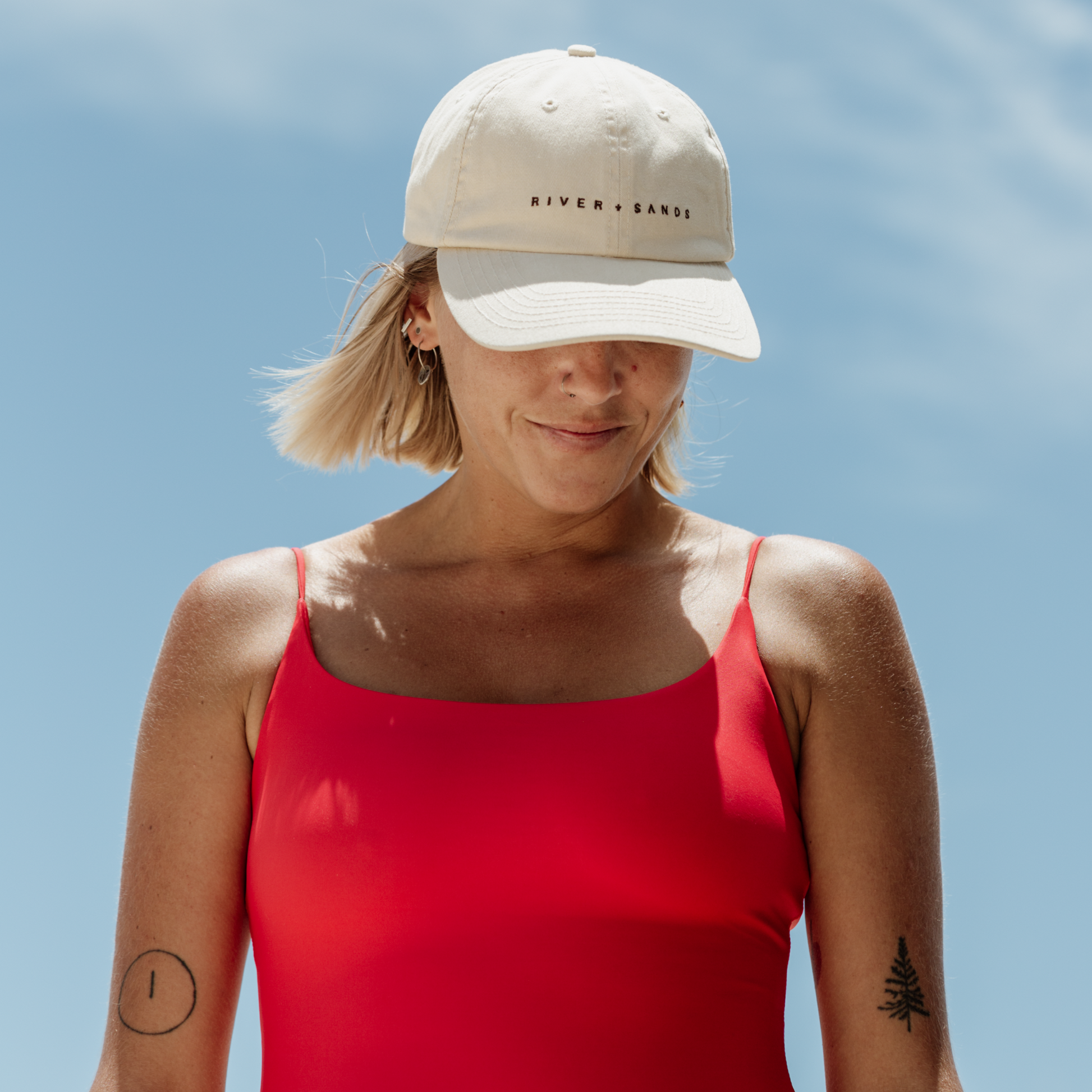 Woman wearing the beige southern Dad Cap with brown embroidery saying river and sands.