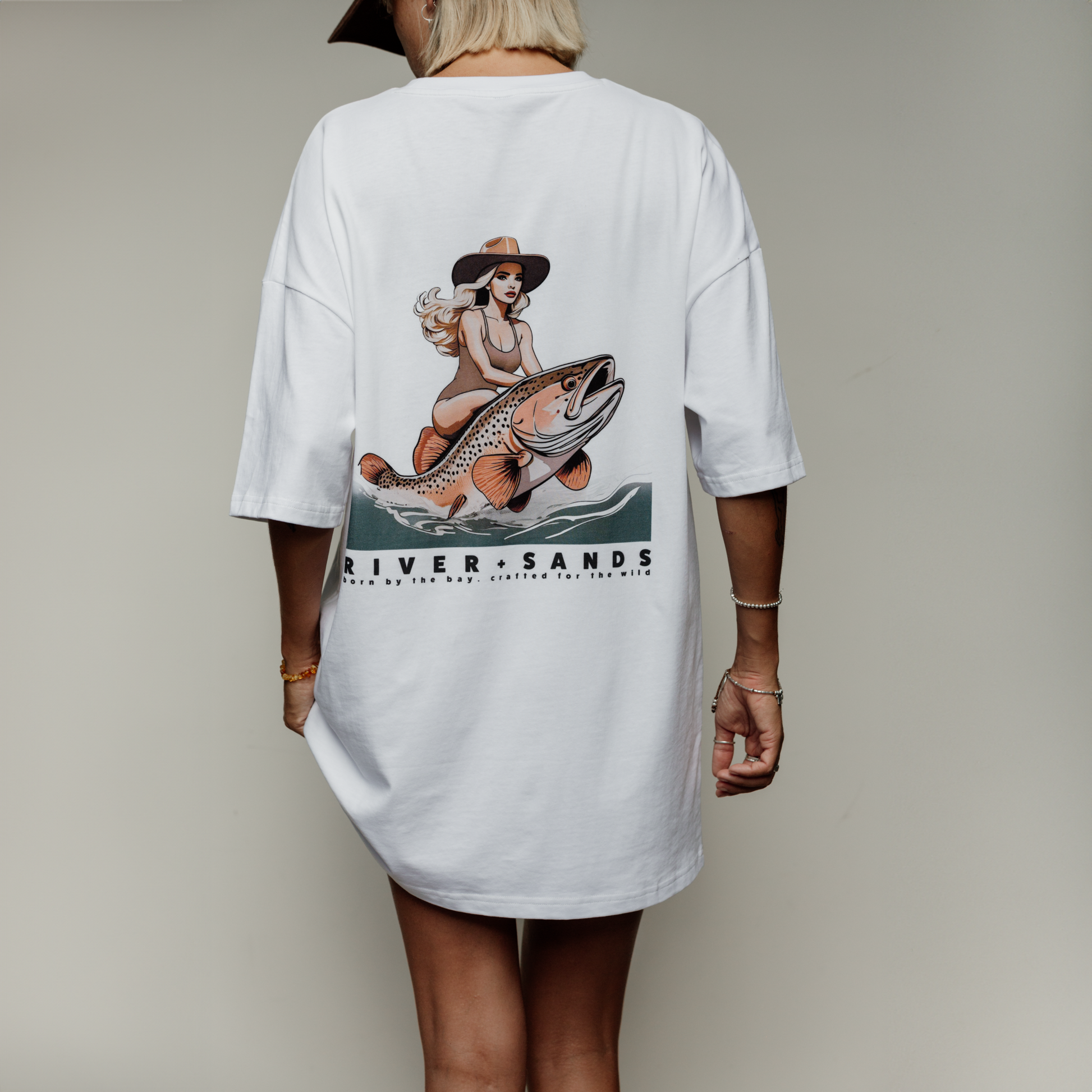 Woman wearing over sized white river and sands t-shirt view of back. Logo is a woman riding a rainbow trout.