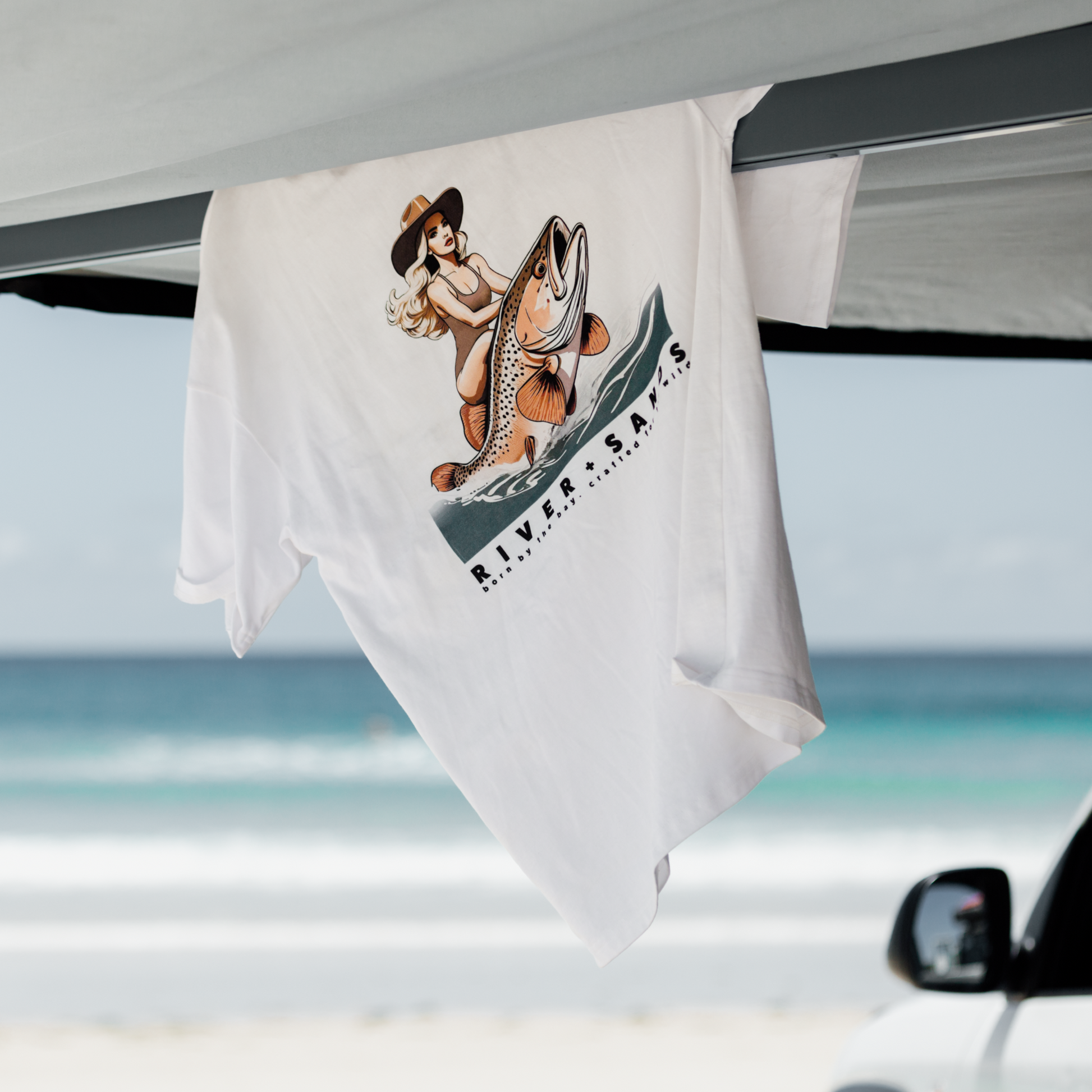 The white salty wrangler t-shirt hanging over a car awning at the beach.