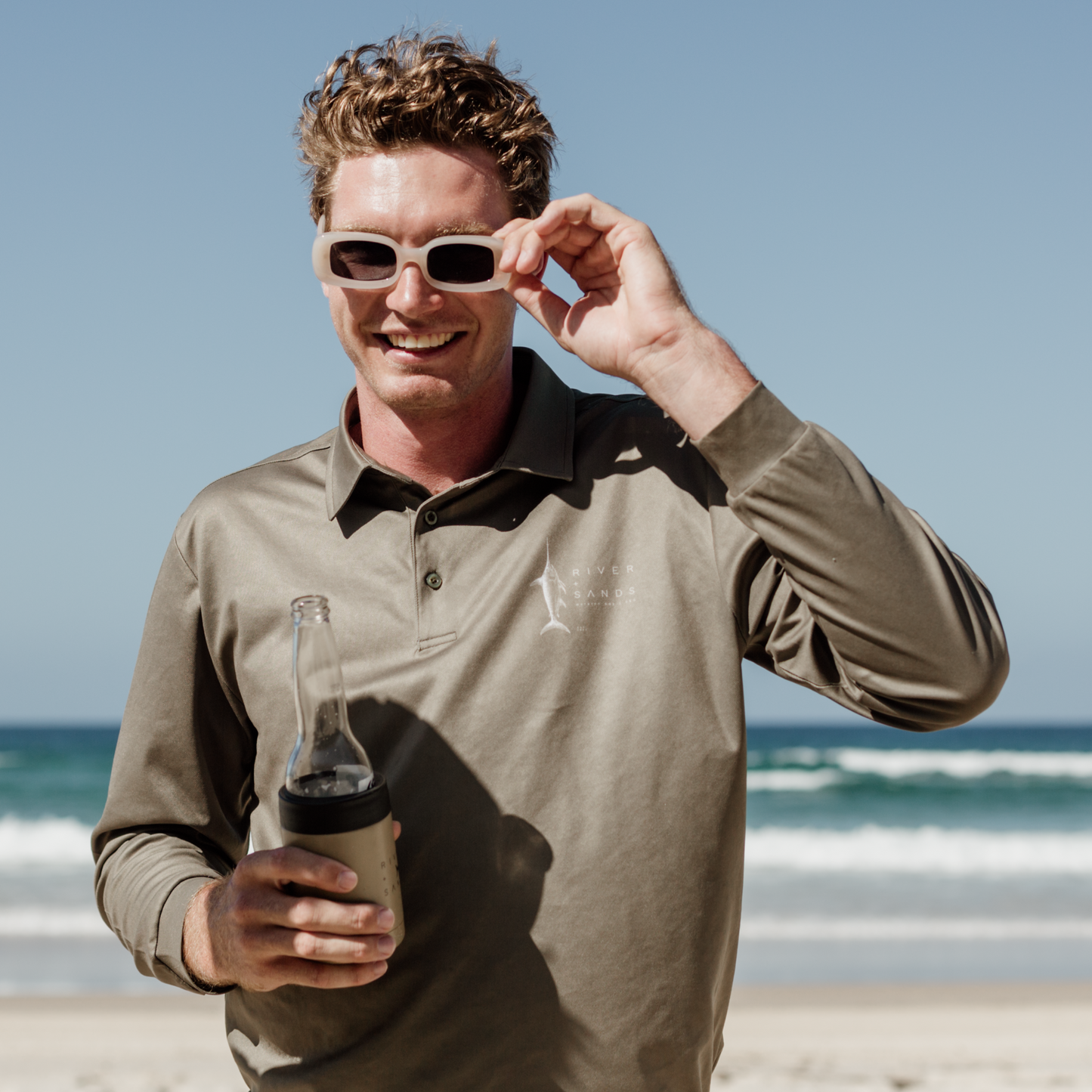 Man wearing the Sands Fishing Shirt polo on the beach with a drink.