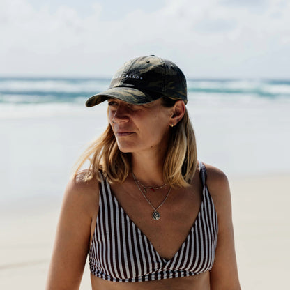 Woman wearing a striped bikini top and camo cap on a beach