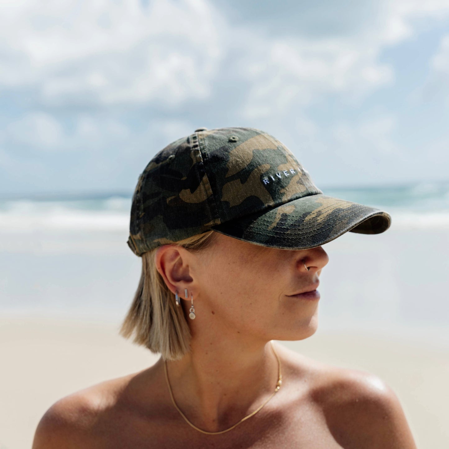 Person wearing a camouflage cap on a beach with ocean and sky in the background